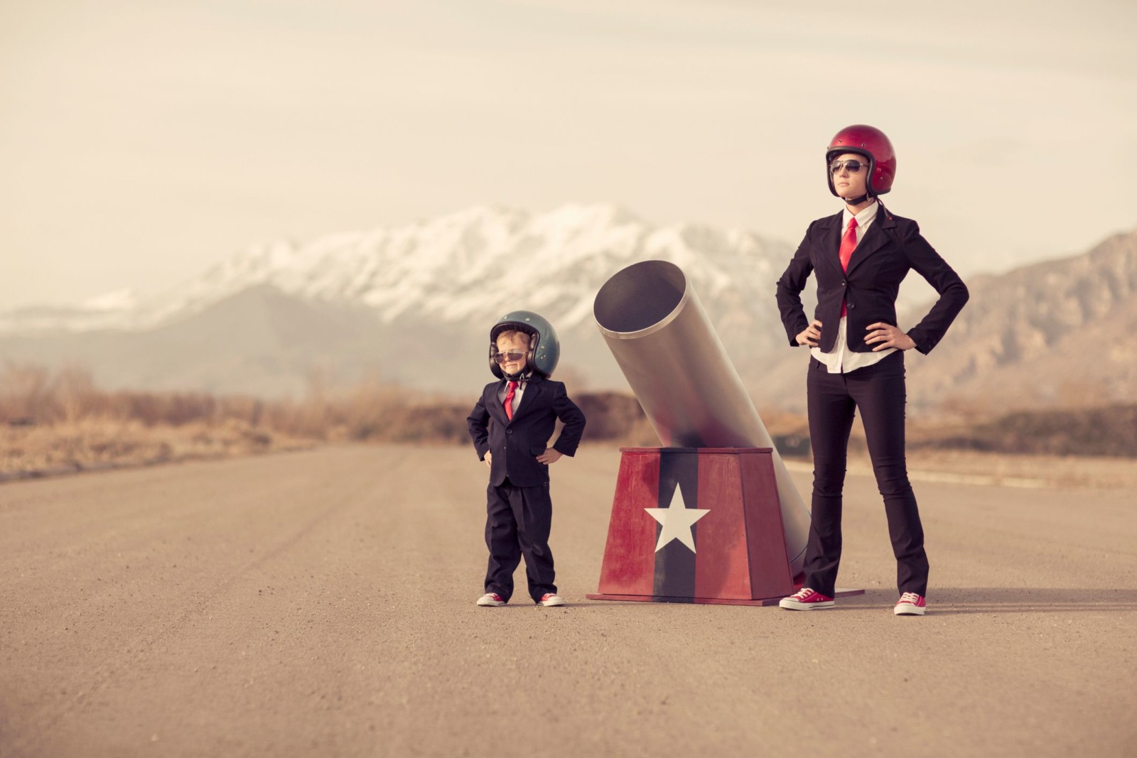 Woman and child in business suits and sunglasses stook either side of a circus cannon