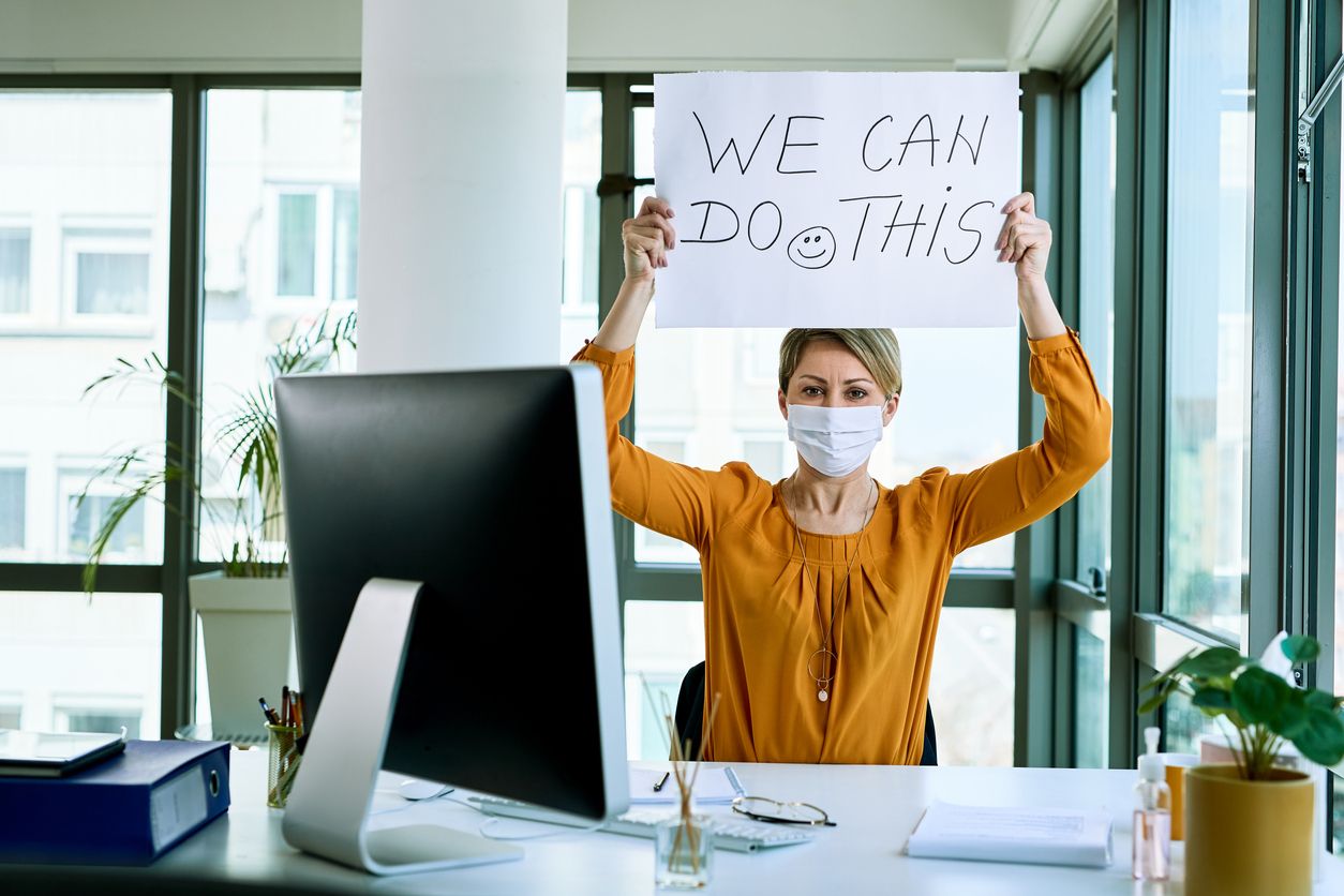 Woman holding a sign in an office saying we can do this